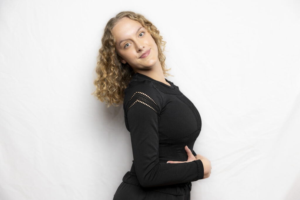 Miss Madeline headshot. Wearing black top in front of white wall